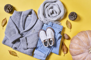 Baby autumn wear clothes on yellow background. Top view. Overhead view of warm kid autumn clothes on colored backdrop