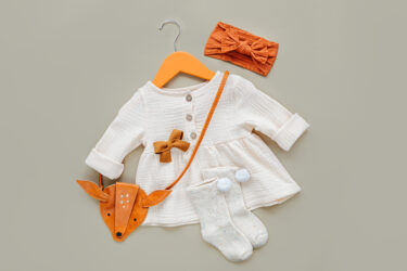 White dress with kids handbag on hanger and socks. Set of baby clothes and accessories for spring, autumn or summer on pink background. Fashion childs outfit. Flat lay, top view